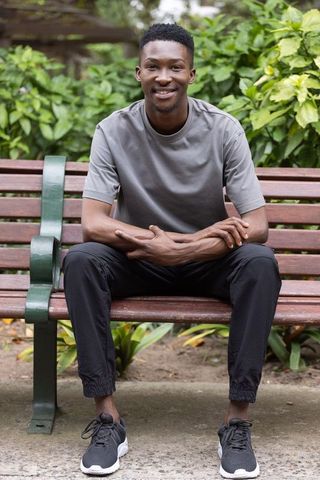 Smiling african man sitting on park bench wearing grey tee and black joggers