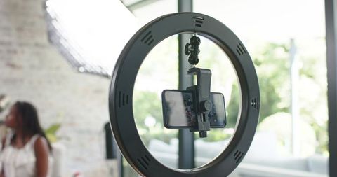 Ring light with smartphone clamp in bright studio, african american women creating content