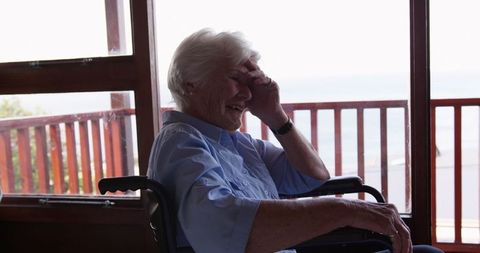 Senior woman sitting in wheelchair appearing worried looking out window