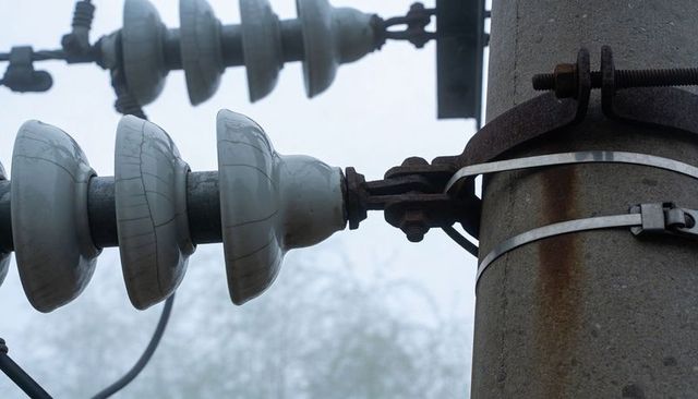 Porcelain insulators cracking on foggy power pole with rusted clamp