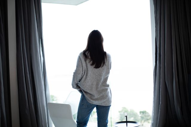 Rear view of a Caucasian brunette woman wearing a grey turtleneck sweater, standing on a balcony, looking away