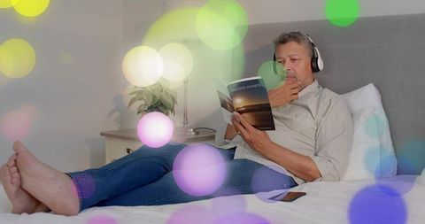 Middle-aged man reading on bed wearing headphones relaxing with colorful bokeh lights