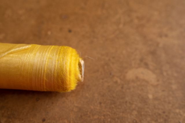 Close up of bobbin of yellow thread in the foreground lying on a brown surface in the workshop at a hat factory.