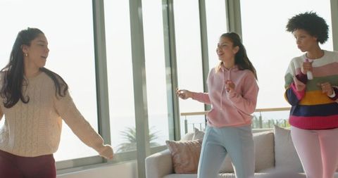 Sunlit seaside apartment friends dancing and laughing in cozy sweaters holding remotes