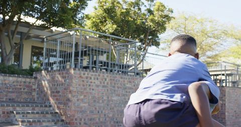 Teen boy giving piggyback to classmate on school courtyard steps, sunlit campus fun