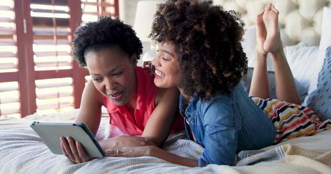 Happy Friends Using Tablet on Bedroom Bed for Leisure and Fun