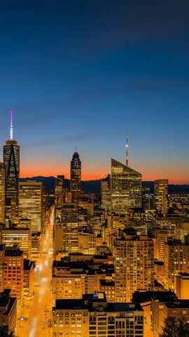 Vertical dusk skyline reveal zooming from rooftop to illuminated avenue and skyscrapers
