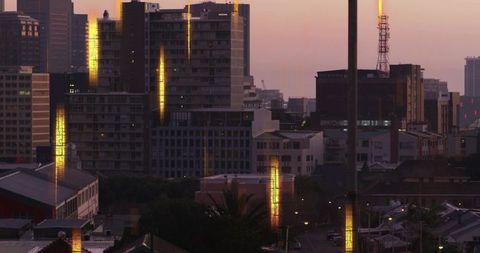 Golden reflections on urban glass towers at dusk with antenna, streetlights and palms