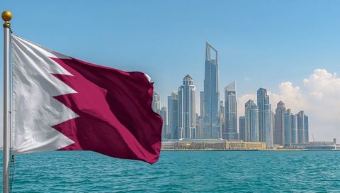 Qatar Flag Billowing Over Doha Marina Skyline With Turquoise Gulf Waters