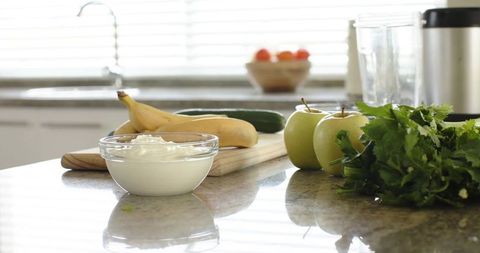 Preparing healthy breakfast: yogurt, bananas, apples and fresh herbs on countertop