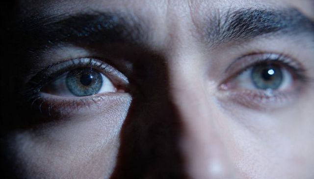 Intense green-blue eyes in dramatic split lighting, close-up portrait with textured skin