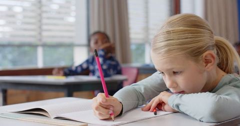 Focused Schoolgirl Writing with Notebook in Classroom