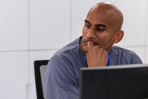 Pensive african professional leaning on hand studying computer monitor at office desk