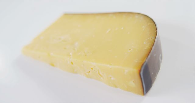 This high-resolution photo showcases a close-up view of a wedge of aged Gouda cheese on a white background. It captures the texture of the cheese with its slightly crumbly surface and fine specks. Perfect for use in culinary blogs, food magazines, or recipe websites. Ideal for marketing gourmet cheese products and highlighting cheese in food photography or culinary education.