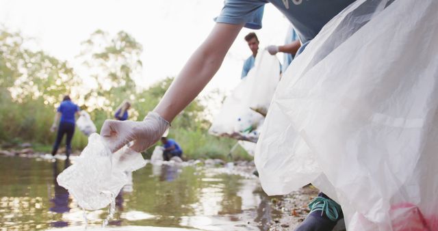 Caucasian woman and group of volunteers cleaning up a river on a sunny day in the countryside, picking up rubbish. Ecology and social responsibility in a rural environment.