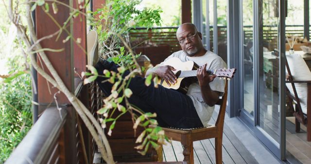 Thoughtful african american senior man sitting on balcony playing acoustic guitar - Download Free Stock Photos Pikwizard.com