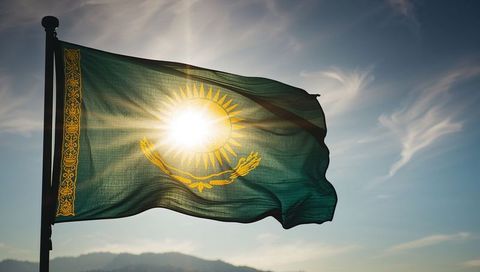 Waving emerald flag with golden sun and eagle motif at hilltop backlit by sun