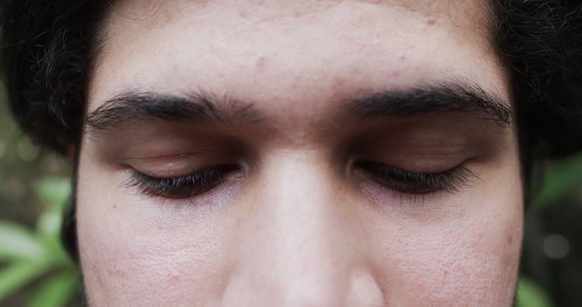 Close-up shot of a young man's face showing closed eyes and defined eyebrows. His skin texture and eyelashes are also visible. This image can be used for projects related to relaxation, meditation, skincare, and emotional introspection.