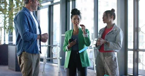 Diverse team collaborating in modern workplace, holding smartphone, wearing casual attire