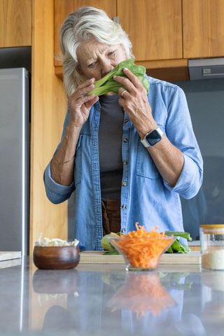 Senior woman sniffing fresh leafy greens while preparing vegetables in cozy kitchen