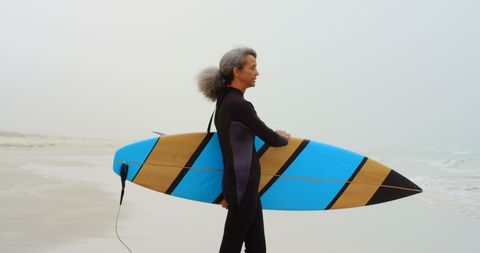 Active senior african american woman with surfboard on beach