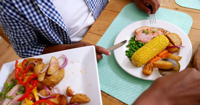 Meal consisting of grilled meat, roasted potatoes, corn on the cob, peas, carrots on wooden table-. Ideal for ads or articles focusing on family bonding through meals, healthy eating habits, or home-cooked food. Great for blogs, websites, and social media content promoting wholesome family dining experiences.