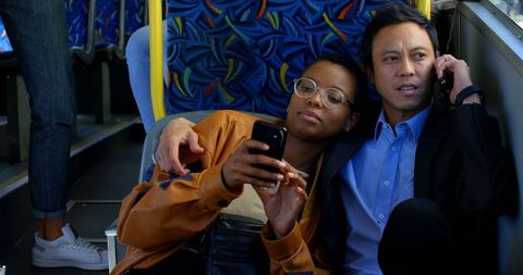 Diverse couple embracing on city bus with smartphones