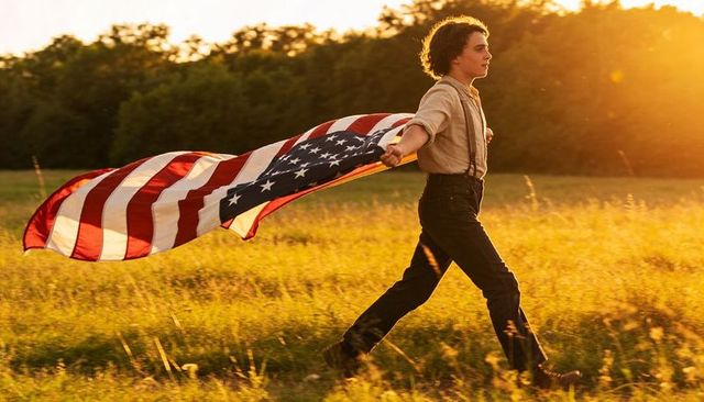 Striding teen holding american flag through golden field at sunset patriotic freedom