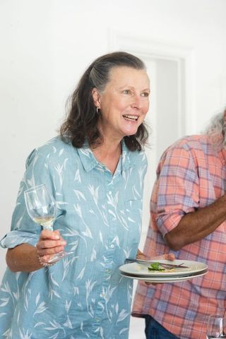 Mature woman smiling and holding wine glass with indian senior at home dinner gathering