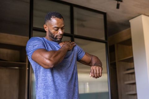 African american man checking shoulder and wrist in dressing room preparing for workout