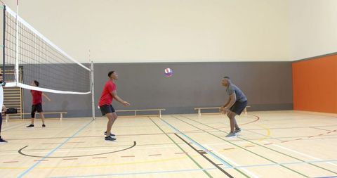 Diverse male athletes playing volleyball in school gym practicing team passing and bumping