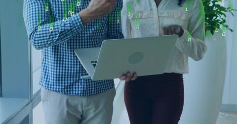 Collaborating professionals reviewing code on laptop with code overlay in office hallway