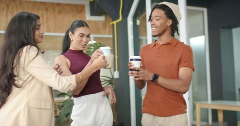 Diverse coworkers clinking reusable coffee cups and chatting in modern office lounge