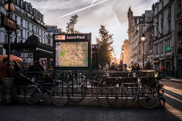 Saint-Paul metro station entrance during sunset with bustling people and parked bicycles. Architecture and historical buildings typical of Paris visible. Perfect for depicting city life, urban exploration, transit themes and travel in a European city.