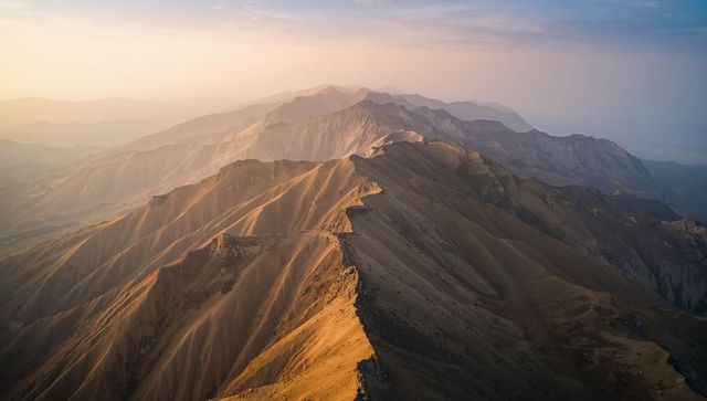 Aerial ridge crest stretching across jagged escarpments and gullies into pastel horizon