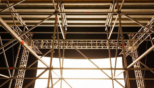 Metal stage scaffolding framing illuminated led backdrop, truss rigging under night sky