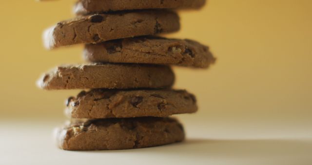 Stack of chocolate chip cookies on light surface with yellow background. Perfect for bakery advertisements, dessert menus, and food blogs showcasing sweets and baked goods.