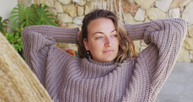 Young woman enjoying her time in a hammock, wearing a cozy sweater and looking relaxed. Suggests ideas of peace, leisure, and comfort. Ideal for content related to relaxation, outdoor living, and lifestyle.