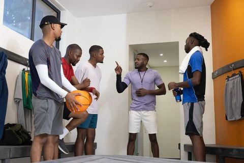 Coach pointing while african american basketball players listening in locker room huddle