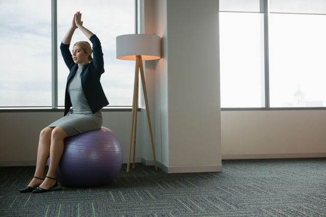 Executive meditating on fitness ball in office