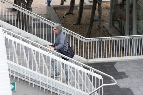 Senior man climbing urban stairway while checking smartphone, carrying shoulder bag