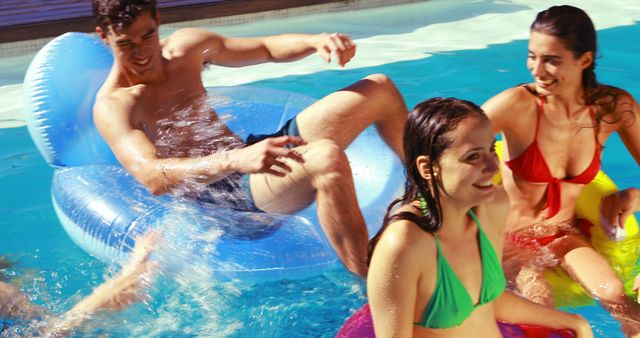 Young adults are enjoying a pool party. They are having fun with swim floats in the bright sunlight. Ideal for use in summer vacation advertisements, promotional materials for pool parties, and leisure-focused marketing campaigns.