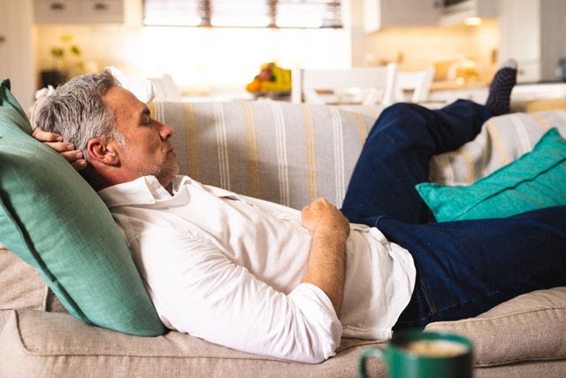 Middle-aged Caucasian man lying on a couch in a cozy living room. Ideal for use in lifestyle blogs, articles about home comfort, relaxation tips, or advertisements for home furnishings and decor.