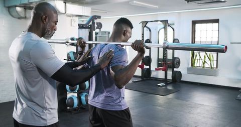 Personal trainer guiding client in barbell squat exercise at gym