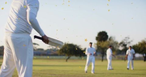 Batsman holding wooden cricket bat celebrating with gold confetti at local park match