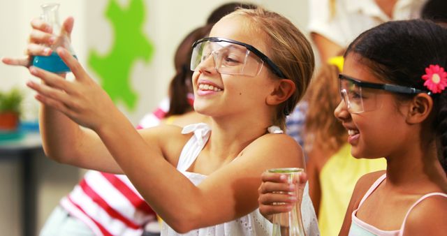 Two young girls, one wearing a white dress and the other tan-skinned, enthusiastically observing a chemical reaction in beakers while wearing protective safety goggles in a classroom. Perfect for use in educational materials, STEM campaigns, advertisements for science programs, or articles promoting diversity in education.