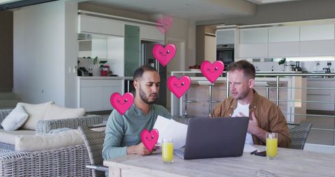Diverse gay couple collaborating on laptop with heart icons