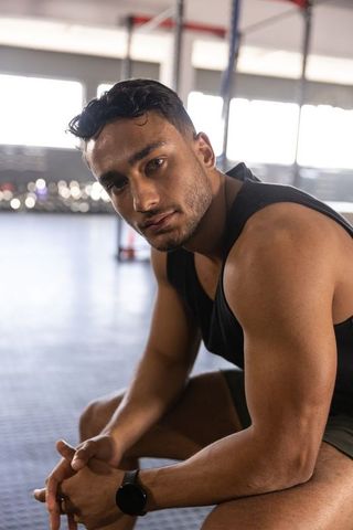 Muscular man checking smartwatch while resting on gym floor near pull-up rig