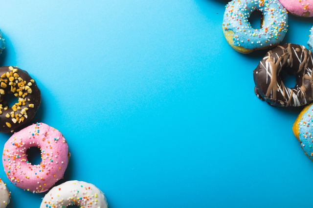 Colorful donuts with various sprinkles arranged on a vibrant blue background. Ideal for use in advertisements, social media posts, and marketing materials related to desserts, bakeries, and celebrations. The bright colors and playful arrangement make it perfect for promoting sweet treats and indulgent snacks.