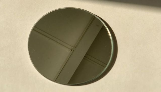 Round mirrored disk reflecting ceiling grid with warm rim light on pale background